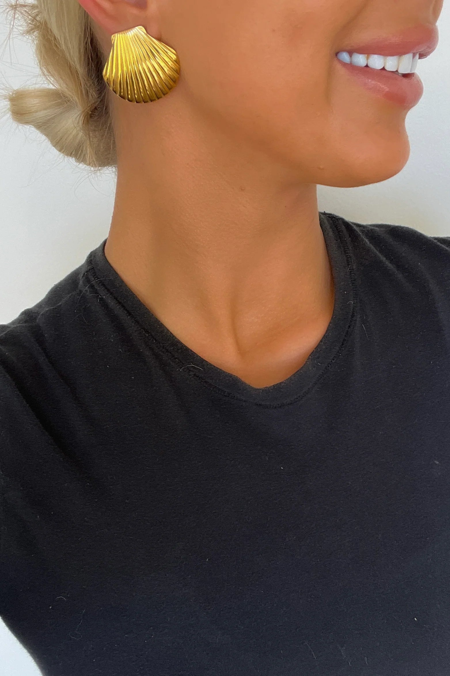 Woman wearing gold shell-shaped earrings against a white background